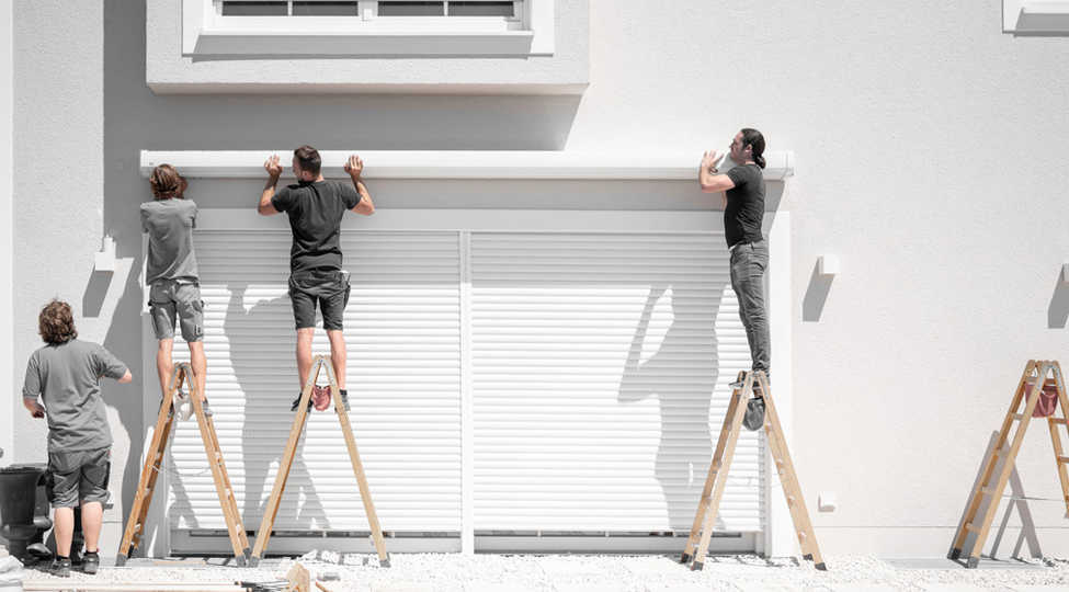 4 Monteure von hinten zu sehen, stehen auf Leitern und montieren den Kasten für eine große Markise an modernes Haus mit weißer Fassade