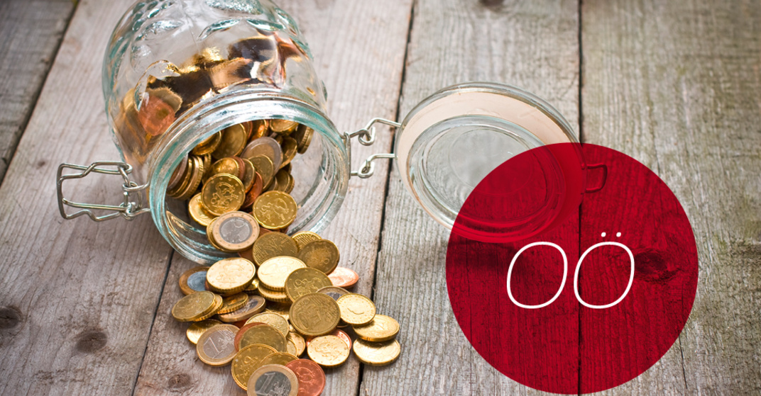 Gekipptes Einmachglas mit verschiedenen Euro- und Centmünzen liegt umgekippt auf einem rustikalen Holzboden, dazu der Text "OÖ" in rotem Kreis. 